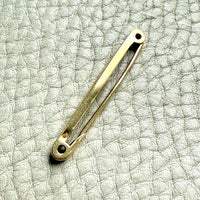 18k gold vintage safety pin brooch on a textured light gray background