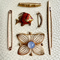 Collection of vintage brooches including a fish, flower, and other designs on a textured white background.
