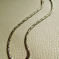 A braided 14k gold chain necklace with laid out on a textured beige leather surface.