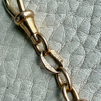 Gold chain pendant detail on a textured light gray background