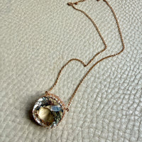 18k gold Necklace with a large, faceted gemstone pendant on a textured beige surface
