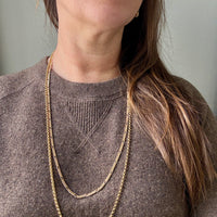 Person wearing gold chain necklaces with a plain background