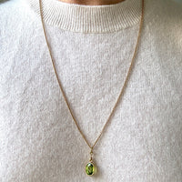 Necklace with a green pendant worn by a person in a light gray sweater.