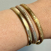 Close-up of a wrist wearing three gold bracelets on a neutral background