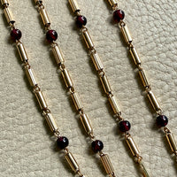 Gold chain necklace with dark red beads on a textured surface