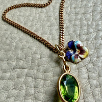 Necklace with a green peridot gemstone pendant and floral charm on a textured surface
