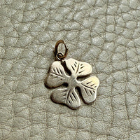 vintage 14k gold four-leaf clover charm on a textured light gray surface