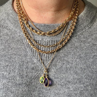 Person wearing multiple gold necklaces with pendant charms on a gray sweater.