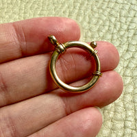 antique 18k gold large bolt clasp held between fingers against a textured light green background