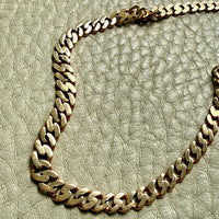 An 18k gold pressed curb link chain necklace draped across a textured light beige leather surface.
