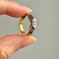 A close-up of a hand holding a two-tone ring with a yellow gold band, a silver-toned textured band, and a clear diamond