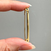 Gold safety pin held between fingers against a gray background