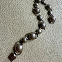 A silver bubble link bracelet with a box clasp on a textured background.
