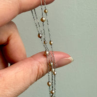 Hand holding a delicate platinum necklace with pearl beads against a plain background