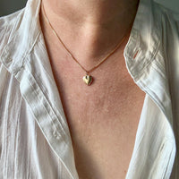 Person wearing a gold necklace with a heart pendant, partially covered by a white shirt.