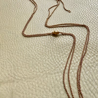 An 18k rose gold victorian chain necklace with a slider central bead detail, laid out on a textured beige leather surface.
