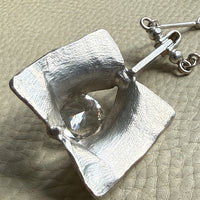 Silver pendant with a clear gemstone on a textured beige surface