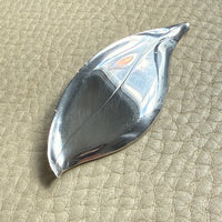 Silver leaf-shaped vintage brooch on a textured beige surface