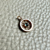 Small round 18k gold vintage pendant with a central blue gemstone on a textured gray surface