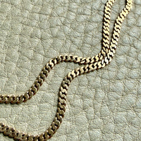 Gold chain necklace on a textured light gray surface