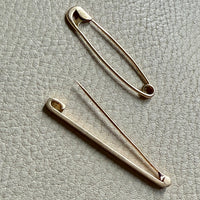 Two gold safety pins on a textured gray surface