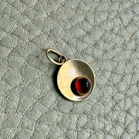 18k gold pendant with an amber gemstone on a textured light gray background