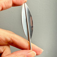 Hand holding a sterling silver leaf shaped brooch against a gray background
