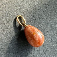 Sunstone teardrop pendant on a gold ring against a gray background