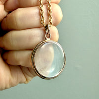 Gold necklace with a round pendant held by a hand against a light green background