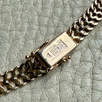 Close-up of a gold chain bracelet with a clasp on a textured light gray surface