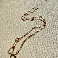 18k gold watch chain necklace with dog clip on a textured light gray background