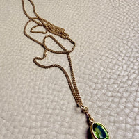 Gold necklace with a green pendant on a textured beige surface