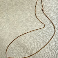 Gold chain necklace on a textured beige surface