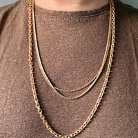 Gold chain necklace on a person wearing a brown shirt against a gray background