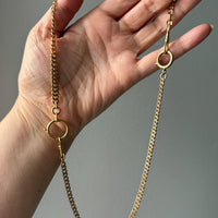 Gold watch chain necklace held in a hand against a gray background. PenelopePenelope.com