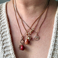 Necklace with charms on a person wearing a beige cardigan against a light blue background