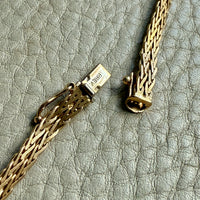 Gold necklace with clasp on a textured gray surface