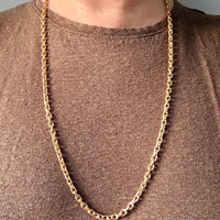 Gold chain necklace on a person wearing a brown shirt