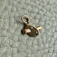 Gold charm resembling a paint palette with red, yellow, and blue dots on a textured gray background
