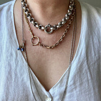 Person wearing multiple gold, silver and platinum necklaces on a plain background