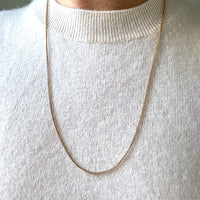Gold chain necklace worn by a person in a white sweater.