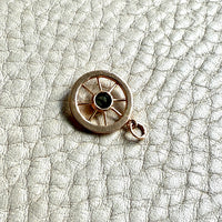 Small round 18k gold vintage pendant with a central blue gemstone on a textured gray surface
