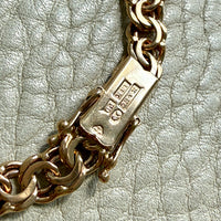 Close-up of a gold chain rectangular clasp with metal hallmarks, resting on a textured light gray surface.