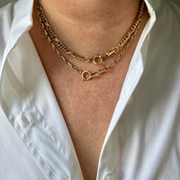 A close-up of a person wearing two layered 18k gold watch chain necklaces over a white button-down shirt.