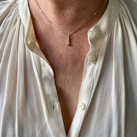 Person wearing a white shirt with buttons undone, revealing a necklace.