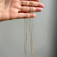 Gold curb necklaces of different lengths held by a hand against a gray background