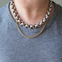 Two chain necklaces on a person wearing a gray shirt.