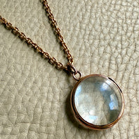glass and gold Necklace with a round pendant on a textured beige background