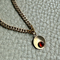 18k gold chain necklace with a round pendant featuring an amber gemstone on a textured gray surface.