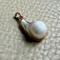 Pearl pendant with gold setting on a textured beige surface